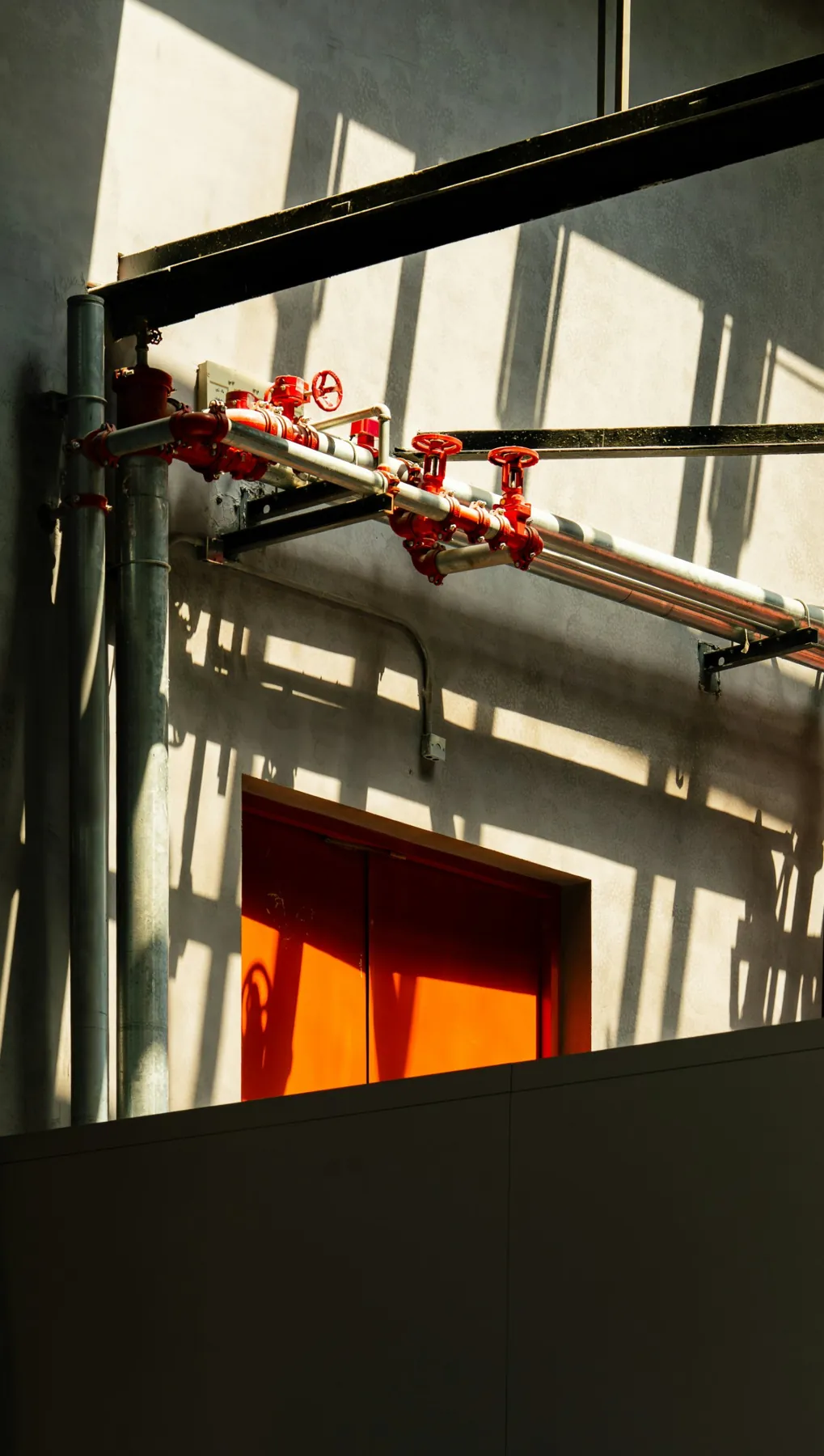 Red control valves on a silver fire sprinkler pipe manifold above an orange door